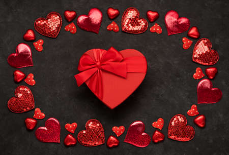 Valentines day gift box over red background and red heart shaped decor. Top view flat lay with copy...