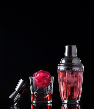 Red drink with ice and bar shaker, black backgroundの写真素材