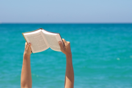 Woman hands holding book and reading on the sea. Conceptual scene. Element of design.の写真素材