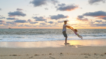 Father and daughter playing together on the sea beach at sunset. Emotional scene.の写真素材