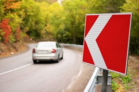 Car on autumn road and red turn sign. Nature and travel scene.