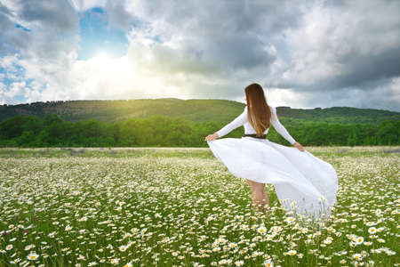 Young woman in a white dress in a field of chamomile flowersの写真素材