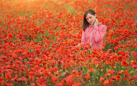 Cute young woman in big meadow of poppies. Emotional and nature scene.