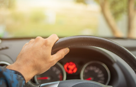 Driver's hands on a steering wheel of and car dashboard.