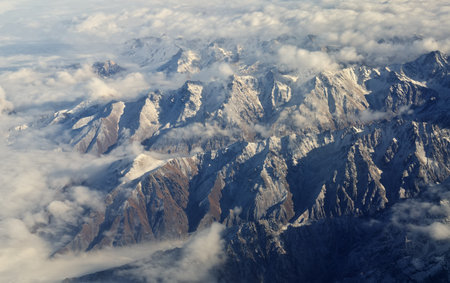 Mountain range and white clouds in blue sky at day. View from above air plane.の写真素材