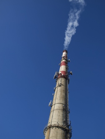 a tall chimney with smoke visible against the blue sky