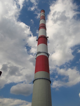 red and white high concrete chimney at a power plant on a background of blue sky with white clouds partially coveredのeditorial素材