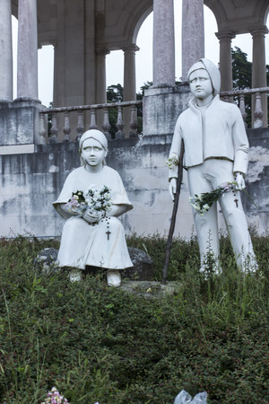 Fatima, Portugal -June 14, 2018: statues of Francisco and Jacinta, the little shepherds who saw the apparitions of Virgin Mary. The colonnade of Sanctuary of Our Lady of Fatima on the background.のeditorial素材