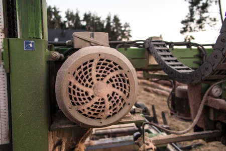 Fragment of mobile sawing equipment for logs in the open air. Rural landscape on a sunny day....