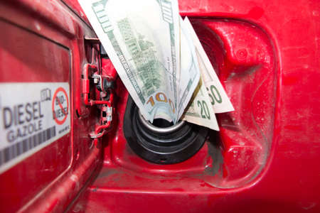 Banknotes, dollars in the fuel filler of a red car. Increase in fuel prices causing money to be sucked into the fuel tanks. The fuel tank sucks moneyの写真素材
