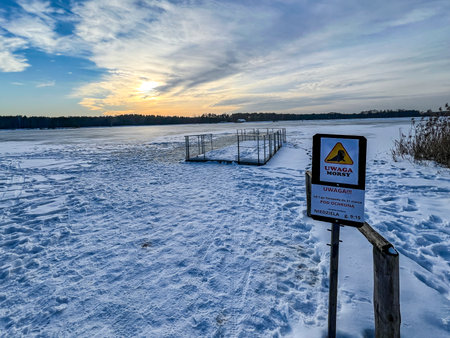 The sun setting over a snow-covered beach and a frozen pond. A boat pulled ashore is visible.の写真素材