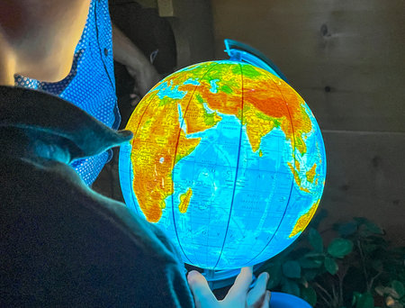 A child curious about the world holds an illuminated globe in his hands.
