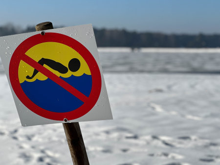 Sign prohibiting swimming by a frozen, snow-covered pond.の写真素材