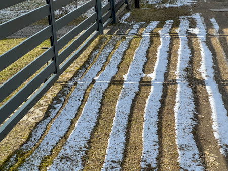 Local melting of snow in a sunny location and snow remaining in the shade. Temperature difference on the ground surface behind a sunny fence.の写真素材