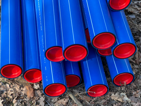 Blue plastic pipes with red caps stored in a forest parking lot.