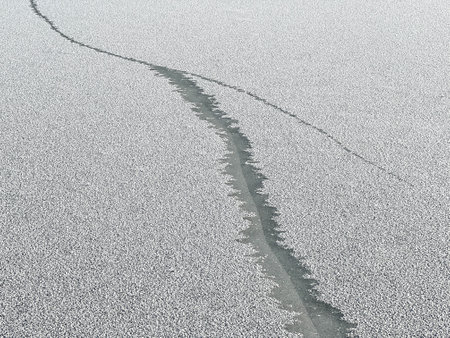 A crack in the ice sheet on a pond lightly covered with snow.の写真素材
