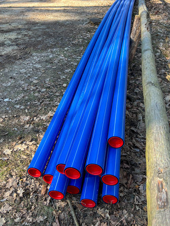 Blue plastic pipes with red caps stored in a forest parking lot ready to be dug into the ground.