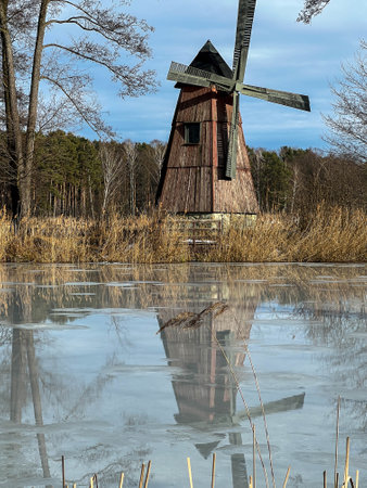 A pond with an island on which there is an old windmill and the surface of the pond water is starting to melt.の写真素材
