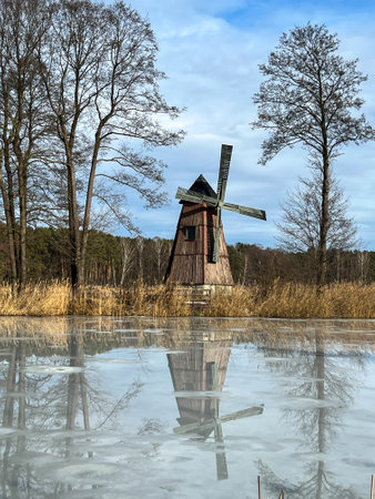 A pond with an island on which there is an old windmill and the surface of the pond water is starting to melt.の写真素材