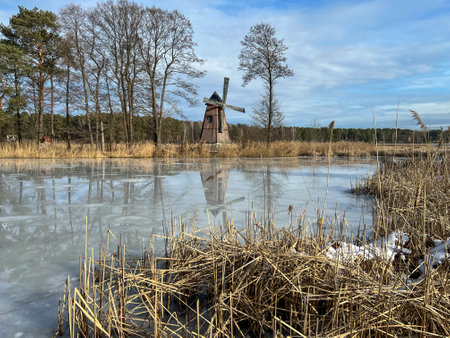 A pond with an island on which there is an old windmill and the surface of the pond water is starting to melt.の写真素材