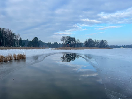 Reflection of trees and an old windmill in the unfrozen part of the water on the lake.の写真素材