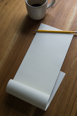 open graph pad with pencil and a cup of coffee on a wooden desk, high angle viewの写真素材