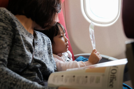 TOKYO, JAPAN - JANUARY 14, 2019: Cute young girl looking at flight safety card with her mom on the airplane flight. Safety on board.のeditorial素材