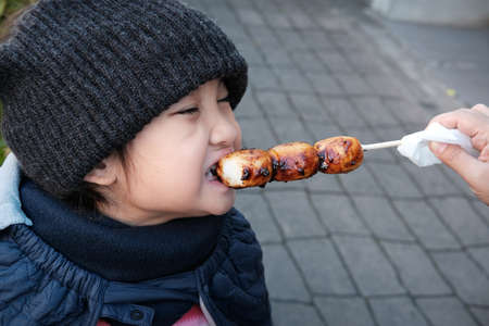 Japan, Kid eating Mitarashi Dango, Traditional Japanese rice dumpling sweet soy glaze. The dumplings...