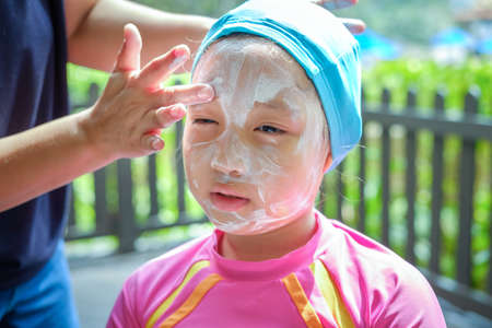 mom applying sunscreen on girl face before swim.の写真素材
