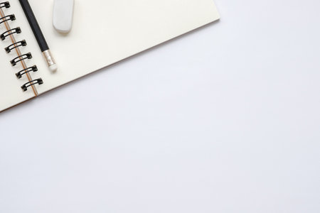 Open blank notebook with pencil and eraser on white background, flat lay, top view of workspace, ...