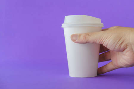 Close up of Man Hand Holding a White Paper Coffee Cup on a Purple Background.の写真素材