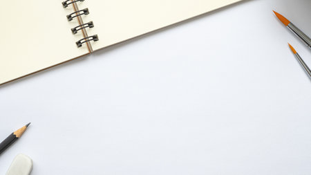 open blank spiral notebook with paintbrush, pencil and eraser on white background, Empty Space for your text, top view of workspace.の写真素材