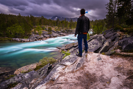 Lofoten Islands - June 16, 2018: Traveler looking at a wild stream passing through the forest in the Lofoten Islands, Norwayの写真素材