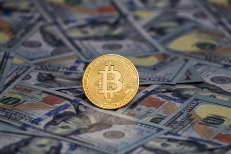 Bitcoin coin on top of 100 dollar bills.