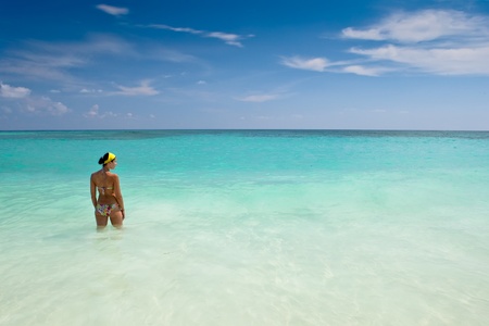 Tanned girls is standing in bright blue ocean under blue skyの写真素材