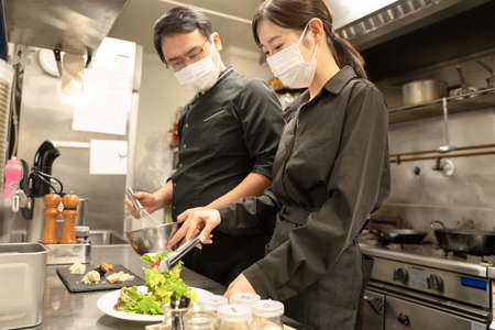 Male and female staff who cook with masks to prevent infectious diseasesの写真素材