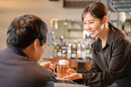 Female staff and male customers serving beerの写真素材