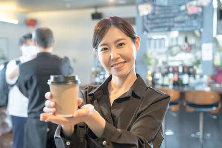 Female cafe clerk handing out takeaway coffeeの写真素材