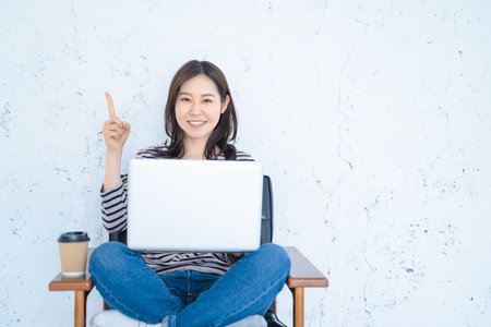 Happy asian woman sitting on chair with laptop and showing thumb upの写真素材