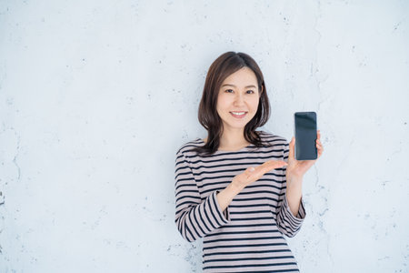 portrait of a beautiful asian woman showing smartphone with blank screenの写真素材