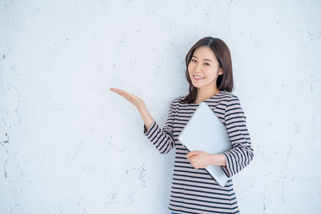 Beautiful asian woman holding laptop computer and pointing on white backgroundの写真素材