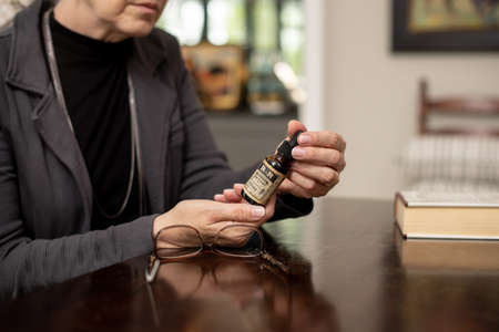 Woman Reading CBD Oil Bottle Label Inside at the Dining Room Tableのeditorial素材