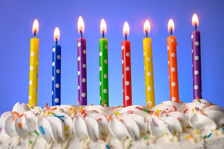 multi-colored candles burn on a birthday cake on blue backgroundの写真素材