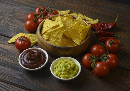 nachos in a wooden bowl and sauces on tableの写真素材