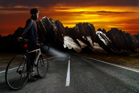 a racing cyclist stands on the street before mountainous region with duskの写真素材