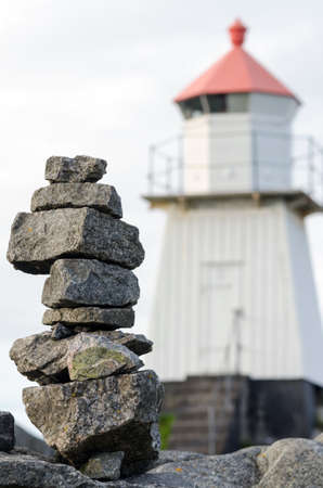 a lighthouse on the coast with a stone heap in the foregroundの写真素材