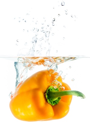 orange pepper falls in the water before white backgroundの写真素材