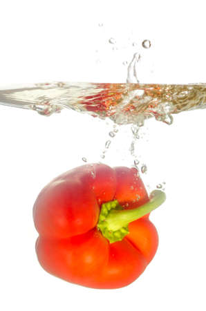 red paprika pepper splashes into water before white backgroundの写真素材