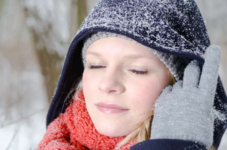 young blond woman smiles with grey beanie and orange scarf in the winter woodの写真素材