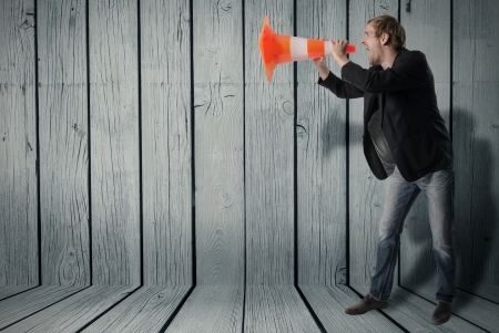 Businessmann uses a warning cone as a megaphone and shouts throughの写真素材